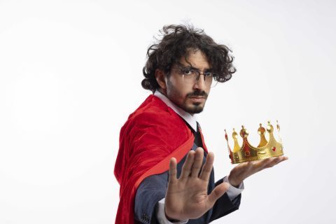 confident-young-caucasian-superhero-man-optical-glasses-wearing-suit-with-red-cloak-holds-crown-gestures-stop-hand-sign_optimized