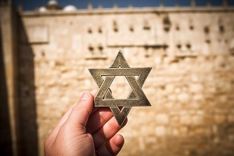 Hand holding a Star of David, a Jewish religious symbol against the Western wall of the Jewish Temple
